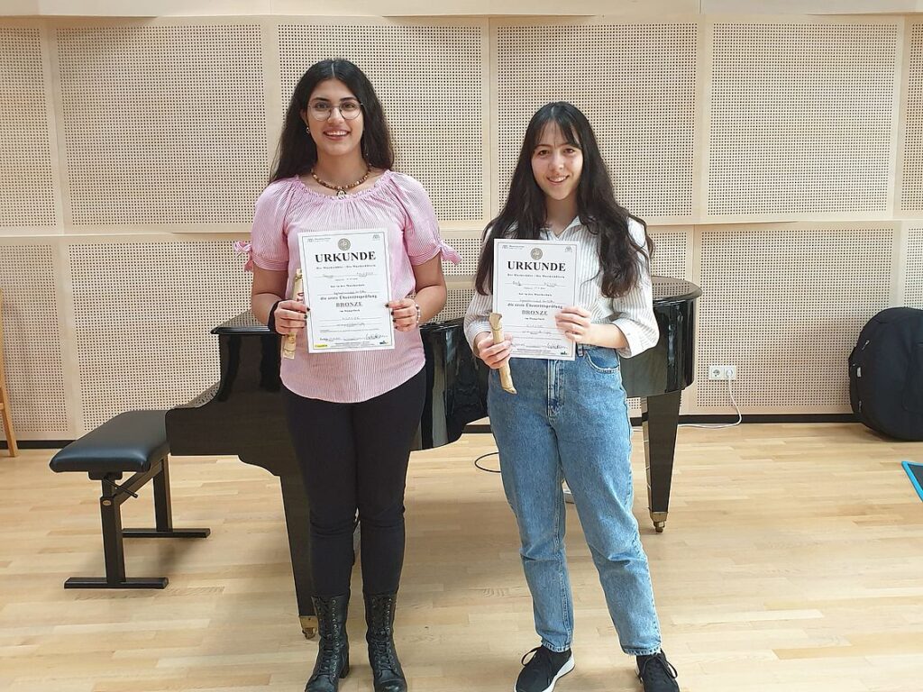 Musikschülerinnen Parmiss Talajooy und Emily Moser mit der Urkunde vorm Klavier